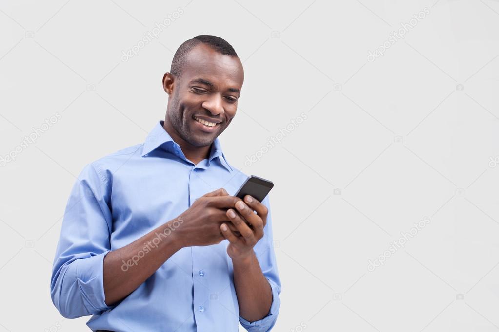 Black man typing something on the mobile phone and smiling