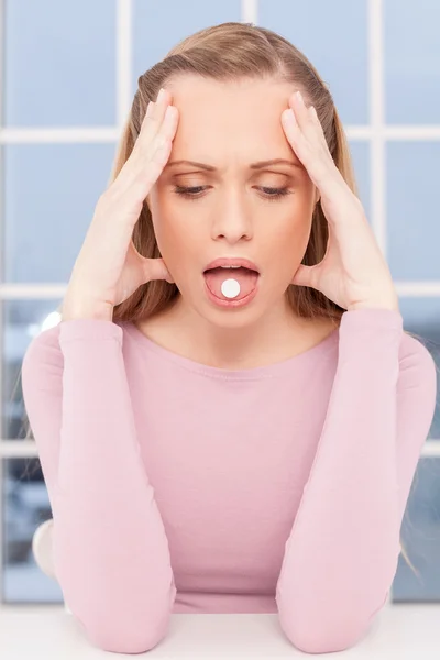 Kranke Frau. Depressive junge Frau berührt Kopf mit Händen und hält Tablette auf der Zunge — Stockfoto