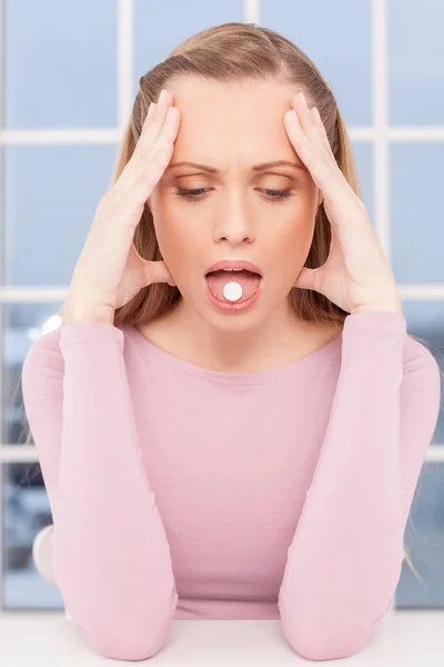 Femme malade. Jeune femme déprimée touchant la tête avec les mains et tenant une pilule sur sa langue — Photo