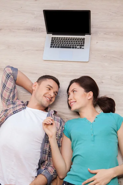 Couple lying down on the floor while laptop lying upon their heads — Stock Photo, Image