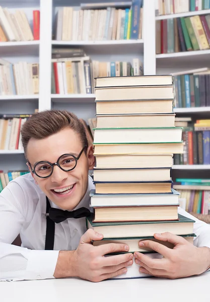 Junger Mann in der Bibliothek und umarmt einen Bücherstapel — Stockfoto