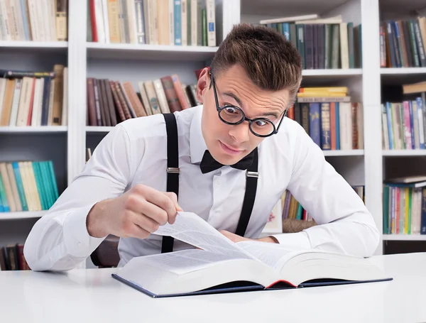 Förvånad ung man läser en bok i biblioteket — Stockfoto