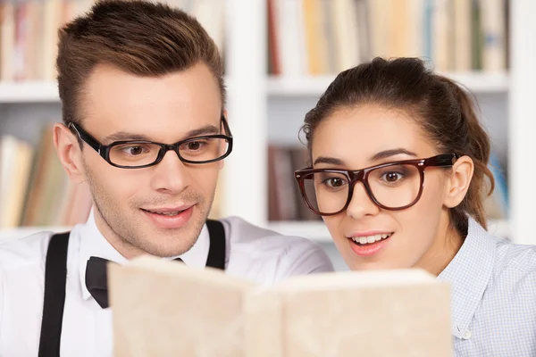Jovem casal nerd excitado em óculos lendo um livro — Fotografia de Stock