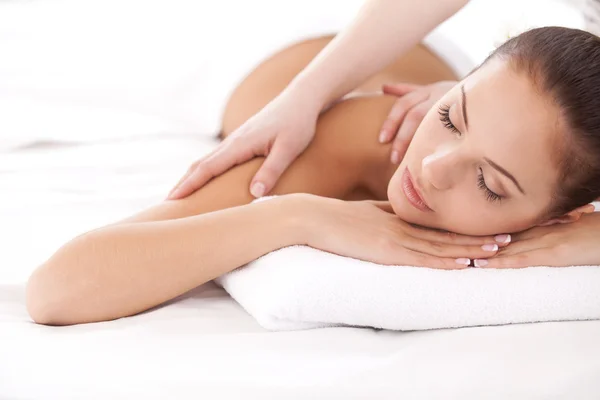 Total relaxation. Beautiful young woman lying on front and looking at camera while massage therapist massaging her shoulders — Stock Photo, Image