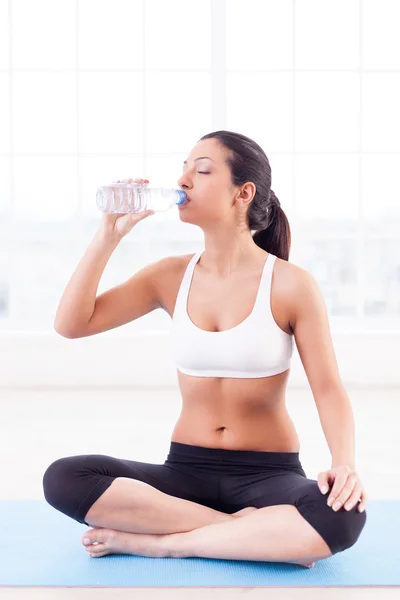 Rehydrating. Attractive young Indian woman sitting in lotus position and drinking water — Stock Photo, Image