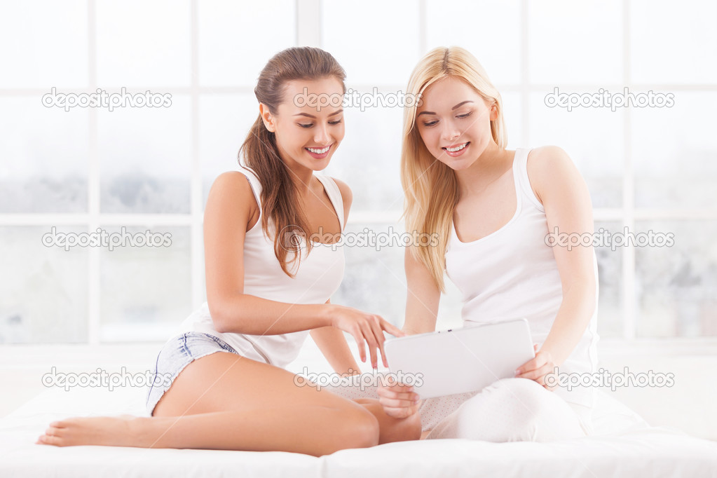 Two attractive young women lying on bed and using digital tablet