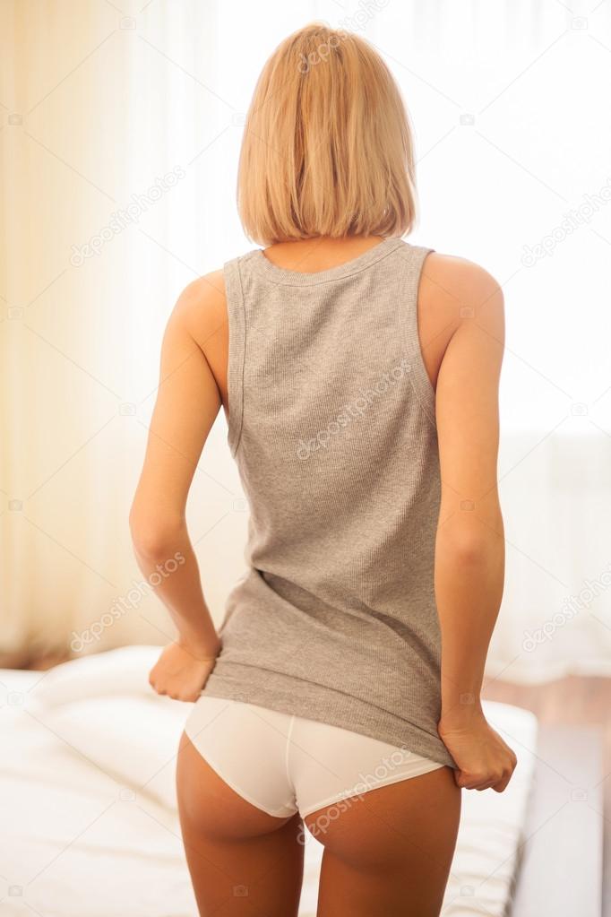 Woman with firm buttocks. Rear view of beautiful young blond hair woman undressing while standing back to camera