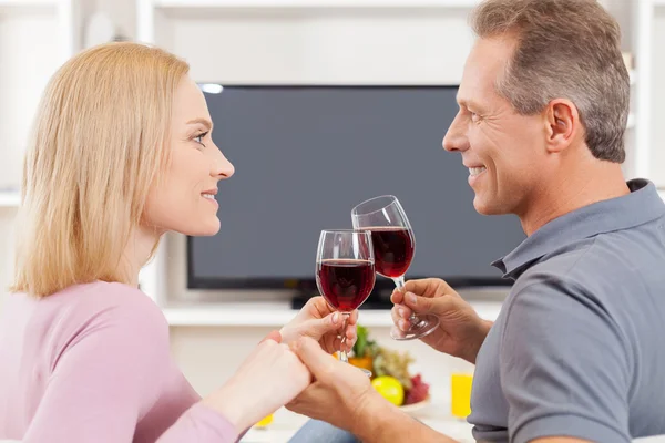 Casal sentado na frente da TV e segurando óculos com vinho tinto — Fotografia de Stock