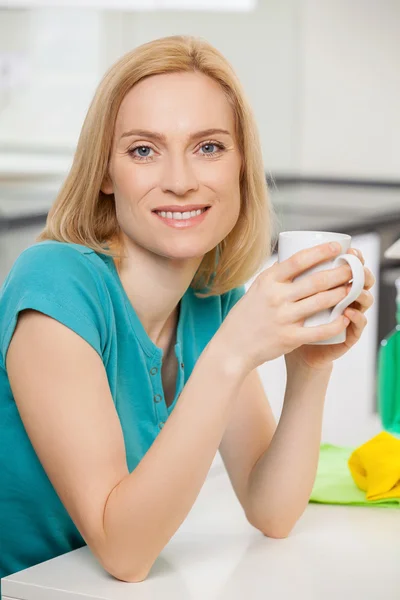 Mulher sentada à mesa e sorrindo com ferramentas de limpeza no fundo — Fotografia de Stock