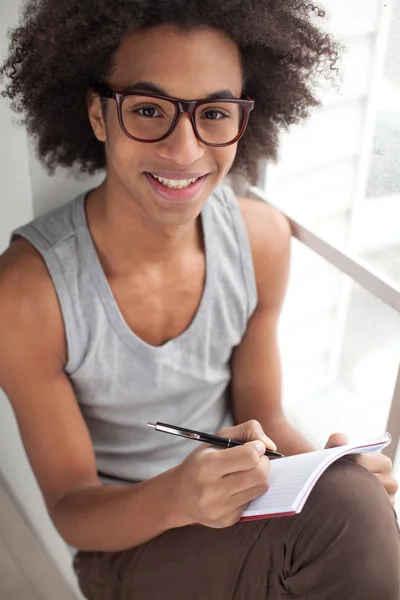 African boy sitting on the window sill holding note pad — Stock Photo, Image