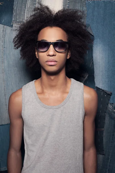 Genial casual. Joven hombre africano en gafas de sol de pie sobre fondo jeans — Foto de Stock