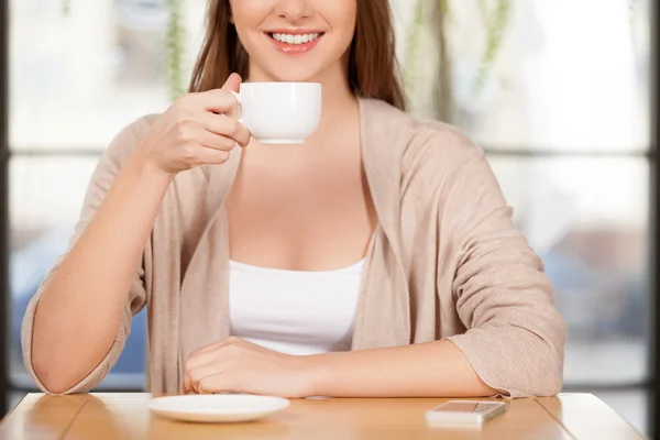 Tomando un café recién hecho. Imagen recortada de la hermosa joven bebiendo café en el restaurante y sonriendo a la cámara —  Fotos de Stock