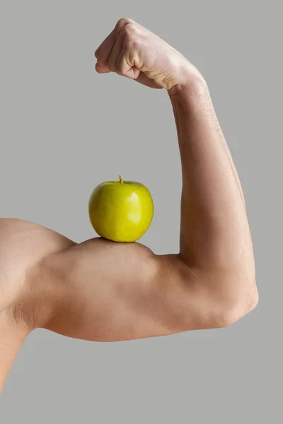 Muscular man showing his perfect biceps with a green apple — Stock Photo, Image