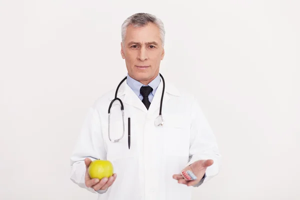 Doctor in uniform holding an apple and pills — Stock Photo, Image