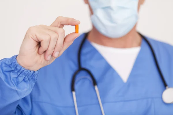 Doctor in surgical mask showing a pill — Stock Photo, Image