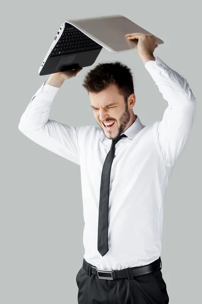 Joven furioso en ropa formal tratando de romper una computadora portátil — Foto de Stock