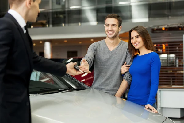 Venditore di auto dando una chiave dalla nuova auto ai proprietari — Foto Stock