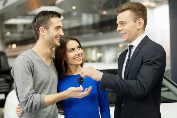 Car salesman giving a key from the new car to the owners — Stock Photo, Image