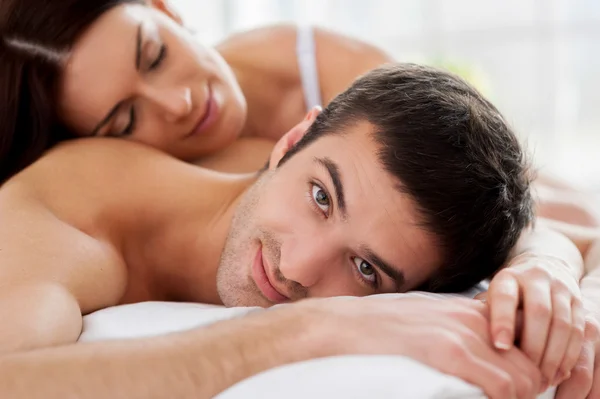 Casal deitado na cama e sorrindo para a câmera — Fotografia de Stock