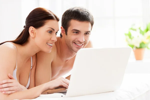 Young loving couple lying in bed and using computer together — Stock Photo, Image