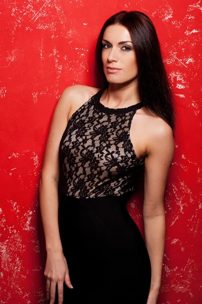 Beautiful young woman in black dress posing against red background — Stock Photo, Image