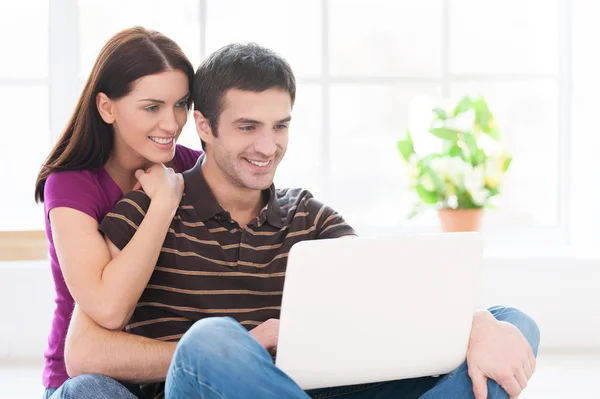 Junges Paar arbeitet zusammen am Laptop, während es auf dem Boden sitzt lizenzfreie Stockbilder