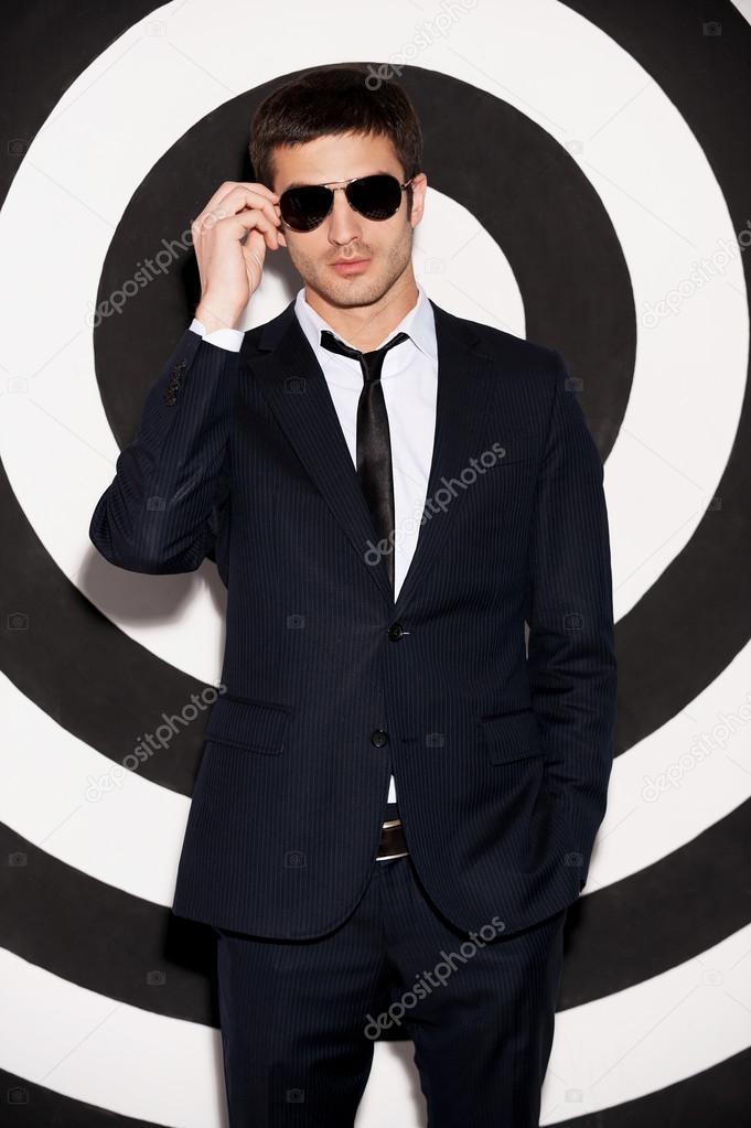 Young man in full suit adjusting his sunglasses