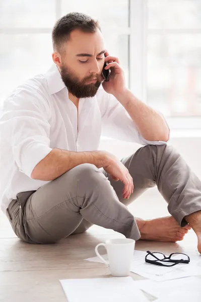 Muž mluví na mobilním telefonu, zatímco sedí na podlaze v jeho bytě — Stock fotografie