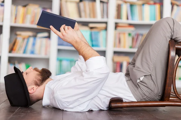 Mann in Hemd und Hosenträgern liegt auf dem Boden und liest ein Buch — Stockfoto