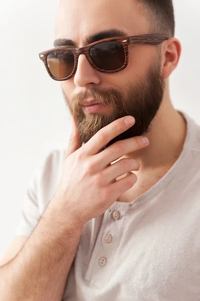 Beau homme aux lunettes de soleil tenant la main sur le menton et détournant les yeux — Photo