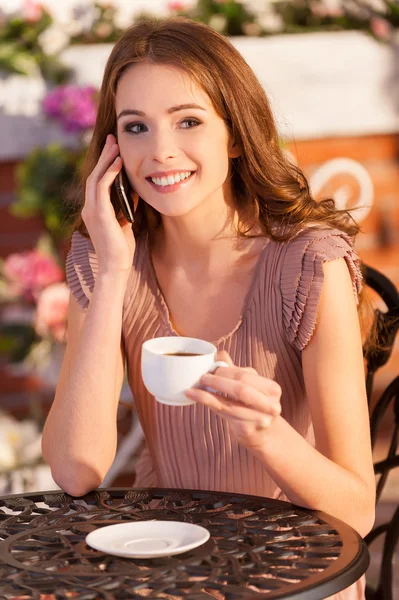 Mulher falando no telefone celular e sorrindo enquanto está sentado no café ao ar livre — Fotografia de Stock