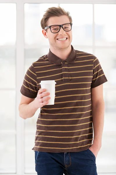Bonito jovem segurando uma xícara e sorrindo — Fotografia de Stock