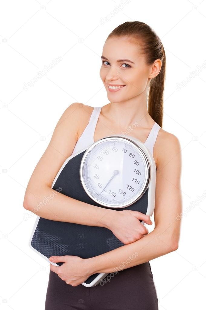 Attractive young woman in sports clothing holding weight scale