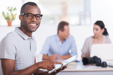 Dijital tablet üzerinde çalışan ve gülümseyerek Afrikalı bir adam