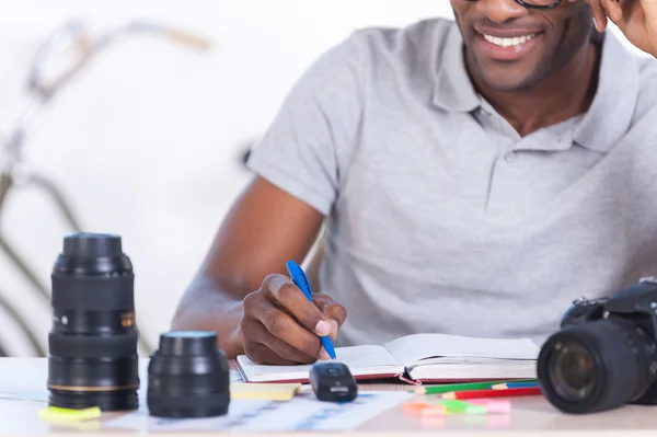 Afrikaanse man zit op zijn werkplek en schrijven iets — Stockfoto