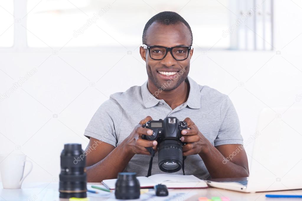 African man sitting at his working place and holding camera