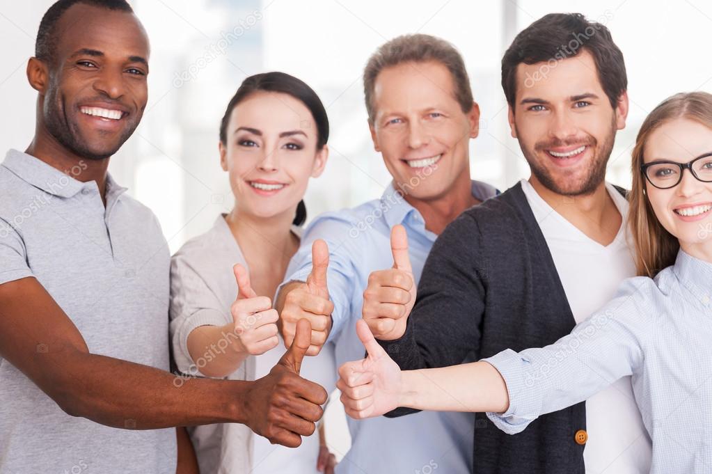 Group of cheerful business people in casual showing their thumbs up