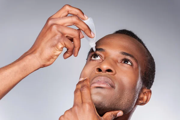 Homem africano aplicando colírio — Fotografia de Stock