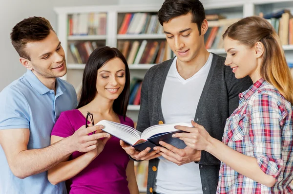 Cuatro estudiantes alegres leyendo un libro — Foto de Stock