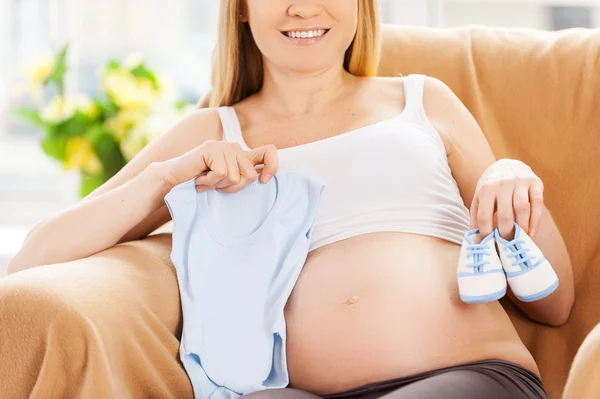 Mulher grávida mostrando roupas de bebê — Fotografia de Stock