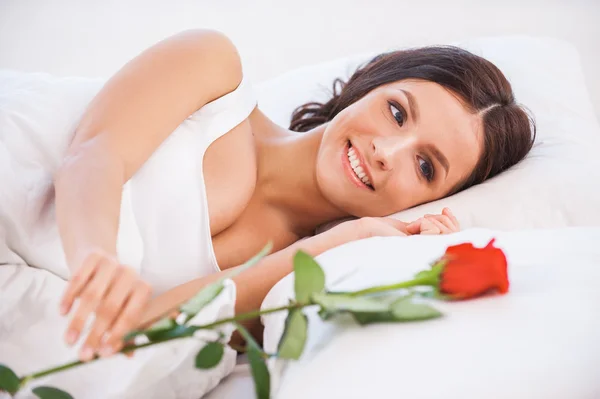 Женщина лежит в постели с красной розой — стоковое фото