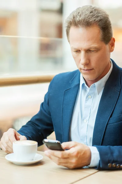 Mature man drinking coffee and typing a message — Stock Photo, Image