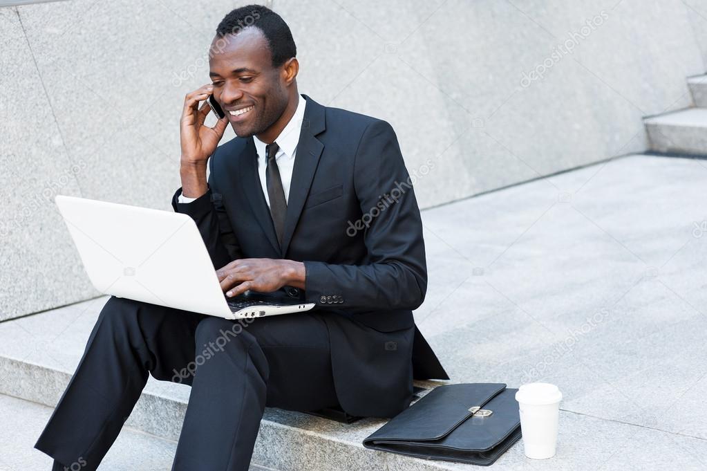 African man talking on phone and working on laptop