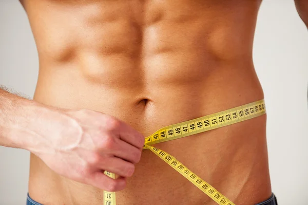 Muscular man measuring his waist — Stock Photo, Image