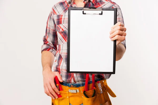 Handyman with tool belt stretching out clipboard — Stock Photo, Image