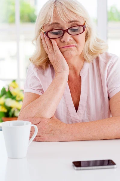 Mulher idosa deprimida olhando para o telefone móvel — Fotografia de Stock