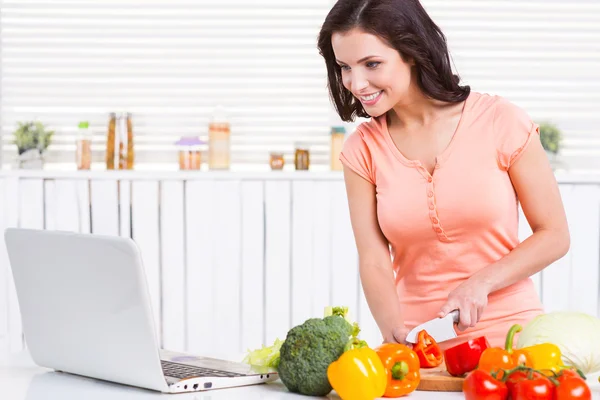 Femme regardant l'ordinateur portable et couper des légumes — Photo