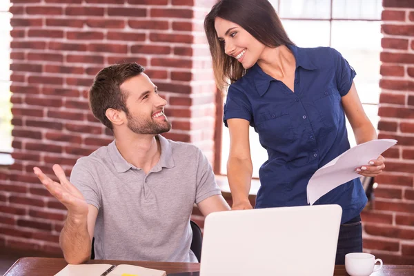 Mann sitzt an seinem Arbeitsplatz und Frau steht — Stockfoto