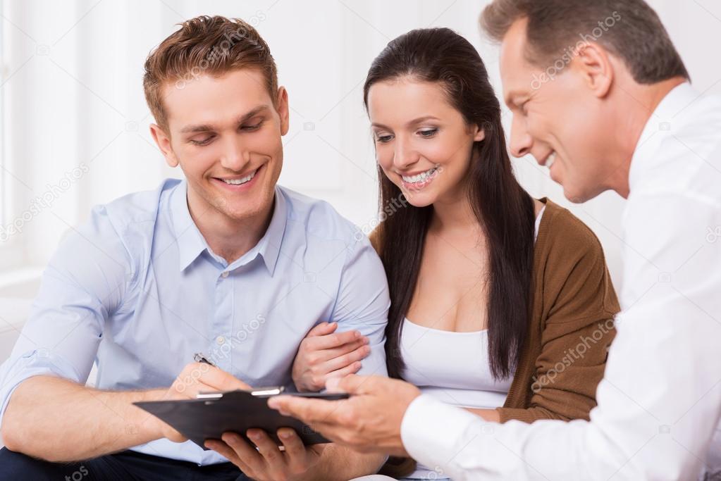 Couple signing documents with man holding clipboard