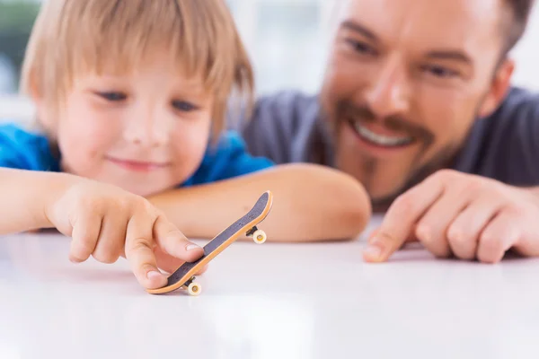 Pai olhando filho brincando com fingerboard — Fotografia de Stock